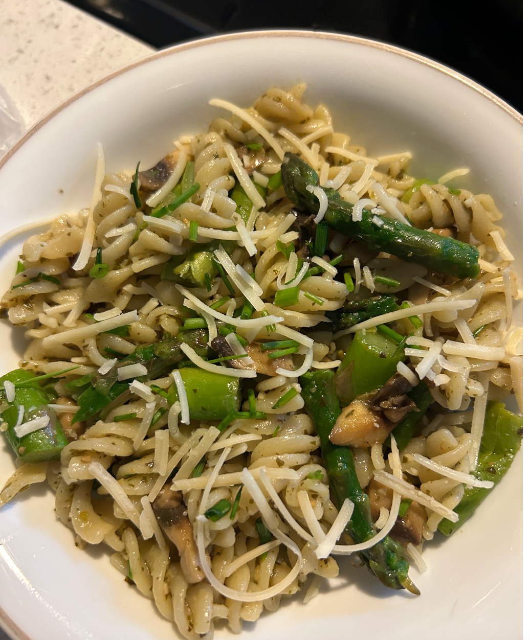 This is a pasta dish with rotini noodles, asparagus, mushrooms, chives, and parmesan cheese. The dish is in a white bowl.
