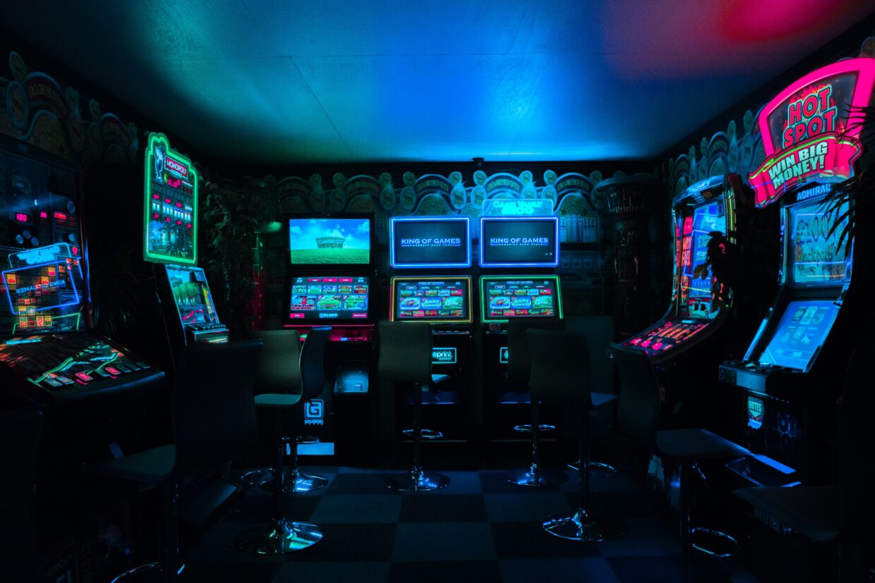Picture of a dimly lit arcade with three arcade machines in the centre. There is also one game to the left of the frame and one to the right.